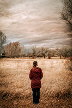 Woman In Long Down Coat In Field Watches Clouds Near Taos, NM