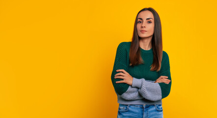 Wall Mural - Close up portrait of gorgeous modern confident brunette woman while she posing in casual clothes with crossed arms on yellow background