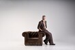 © Friends Stock - Full length shot of fashionable mature man with beard wearing elegant suit looking at camera, leaning on armchair while posing isolated over light background