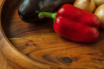 Wall Mural - food background of vegetables in a wooden plate, eggplants, red sweet peppers and onions, healthy lifestyle concept