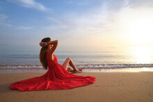 Young Happy Woman In Red Dress Relaxing On Sandy Beach By Seaside Enjoying Warm Tropical Morning