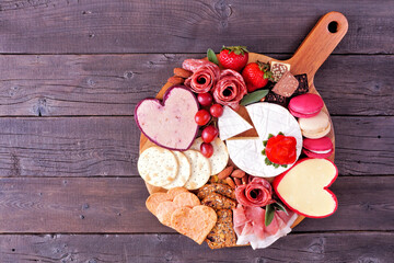 Wall Mural - Valentine's Day theme charcuterie board with a selection of cheeses, appetizers and sweets. Overhead view on a dark wood background.