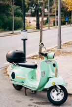 Green Motor Scooter Is Parked On The Street Near The Post