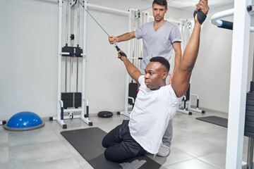 Wall Mural - Concentrated man doing stretching exercise aided by physiatrist