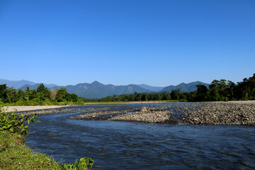  Black water Kameng river flowing through forested valley of Himalaya foothills under bright clouded sky near Bomdila, Arunachal Pradesh, India.