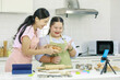 Asian young happy chubby down syndrome autistic daughter wears apron standing smiling laughing in kitchen touching hands with lovely mother when finish bakery lesson. Teacher high five with student