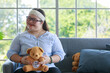 © Bangkok Click Studio - Portrait close up shot of Asian young happy chubby down syndrome autistic autism girl model wearing eyeglasses white knitted headband holding teddy bear doll smiling look at camera in living room