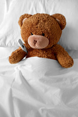 Wall Mural - medicine, healthcare and childhood concept - ill teddy bear toy head with thermometer lying in bed