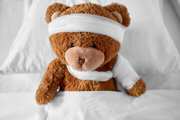 Wall Mural - medicine, healthcare and childhood concept - ill teddy bear toy with bandaged paw and head lying in bed