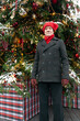 An elderly man in a red, funny hat and coat on the street, near the Christmas tree