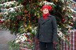 An elderly man in a red, funny hat and coat on the street, near the Christmas tree