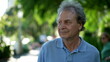 © Marco - Pensive senior man walking outside in city green nature path