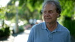 © Marco - Pensive senior man walking outside in city green nature path