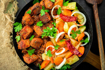 Wall Mural - Stew with meat and vegetables in black iron dish. Traditional  gourmet goulash in a rustic kitchen. Top view