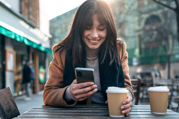 pretty young woman using her mobile phone while drinking cup of coffee in the terrace of a coffee sh