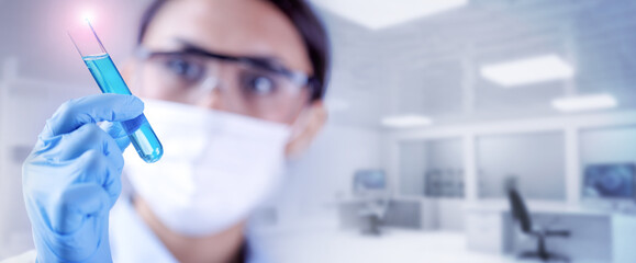 Wall Mural - Blurred female scientist holding a test-tube filled of blue liquid sample in chemical lab. Concept of biochemistry, pharmaceutical or medical research