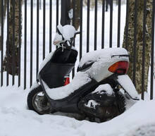 A Snow-covered Black Moped Is Parked At The Black Fence