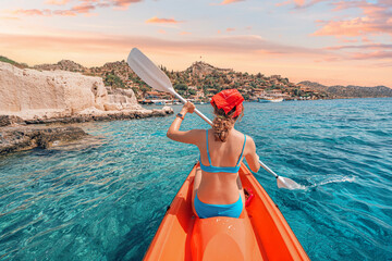 Wall Mural - Happy girl is rowing on a sea kayak near Kekova island with view of Simena Castle and Kaleucagiz village in Turkey. Outdoor recreation and exploration. Travel as a lifestyle