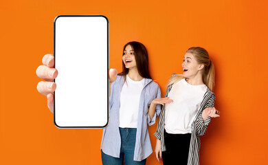 Excited women showing white empty smartphone screen close to camera