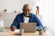 Mature African Businessman Taking Notes Using Laptop Working Online Indoor