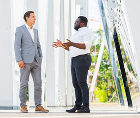 Wall Mural - Finance, business and cooperation concept. Two successful businessmen are talking on the street. Office workers are discussing business issues outdoor.