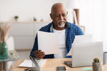 Senior African Businessman Working With Papers Sitting At Laptop Indoor