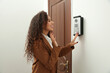 © New Africa - Young African-American woman ringing intercom while waving to camera in entryway