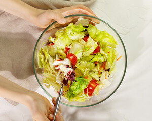 The vegan diet. Healthy food. Children 's hands hold glass bowl with salad with herbs, cherry tomatoes, and olive oil with fork on a blue background with shadows. The concept of simple healthy food