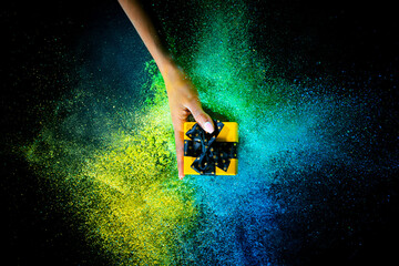 Wall Mural - Female hand and explosion of colored, neoned powder on black studio background with copy space. Magazine cover, wallpaper design