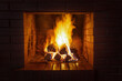 A stack of firewood burns with a bright hot flame in a red brick fireplace on a late dark cold evening