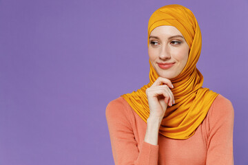 Wall Mural - Pensive wistful young arabian asian muslim woman in abaya hijab yellow clothes put hand prop up on chin lost in thought and conjecture isolated on plain pastel light violet background studio portrait