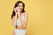 Smiling young european nice fun beautiful brunette woman 20s wearing white underwear brassiere hold in hand flower look aside on area isolated on plain yellow background. People female beauty concept.