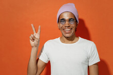 Confident Cheery Excited Cheerful Happy Joyful Young Black Curly Man 20s Years Old Wears White T-shirt Pink Hat Glasses Showing Victory Sign Isolated On Plain Pastel Orange Background Studio Portrait.