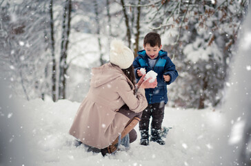 Wall Mural - Young, beautiful mom and her little boy playing in the snow, making snowball