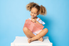 Cute Little Girl Sitting On A Table Writing In Notebook Isolated Over Blue Background. Back To School Concept.