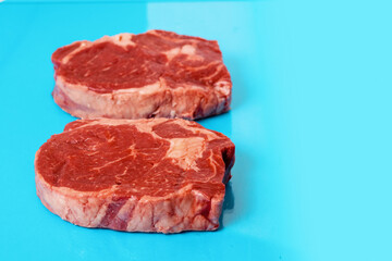 Two fresh juicy rib eye steak on blue surface. Top quality fresh meat. Butcher craft product and meat industry. Rich red color and marbling. Premium cut.