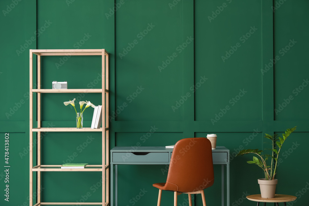 Modern workplace and bookcase with flowers near green wall