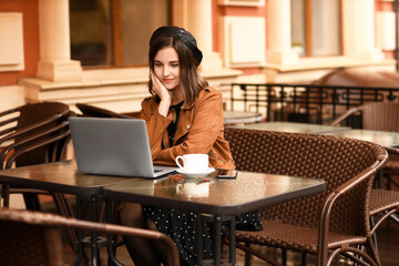 Sticker - Young woman with laptop, mobile phone and cup of coffee in street cafe