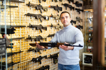 Wall Mural - Man standing in salesroom of airsoft shop and holding assault rifle.