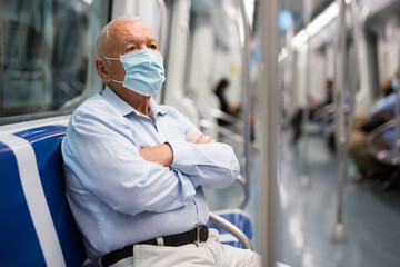 Elderly man in face mask sitting on bench inside subway car and waiting for his stop.