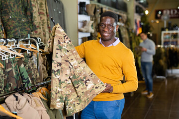 Wall Mural - Adult male shopper chooses camouflage uniform at army store