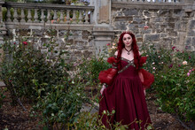  Portrait Of Pretty  Female Model With Red Hair Wearing Glamorous Renaissance Red Ballgown.  Posing In A Fairytale Castle Location With Staircases 