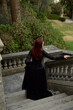  portrait of pretty  female model with red hair wearing glamorous gothic black lace ballgown.  Posing in a fairytale castle location with staircases 