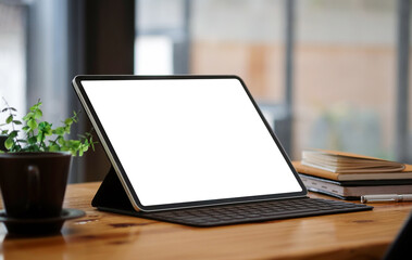 Mock up computer tablet with white display, red coffee cup and books on wooden table.