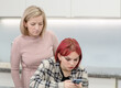 Curious mother  looks at the  screen of smartphone that her teen daughter uses