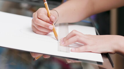 Close-up of young creative artist hand sketching on paper using graphic pencil and ruler for art class homework sitting at desk. Painter kid drawing creative abstract paint. Fun school activity