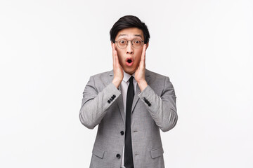 Wall Mural - Waist-up portrait of shocked and amazed young speechless asian male entrepreneur in suit, drop jaw, gasping and saying wow, fixing glasses as cant believe own eyes, stare camera, white background