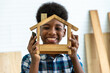Portrait of smiling African black boy child kid carpenter holding a model of wooden house in carpentry workshop. Concept hobby at home.