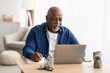 © Prostock-studio - Senior Black Man Using Laptop Taking Notes Working At Home