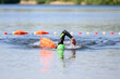 Swimmer swimming outdoor in nature with a green swimming cap and orange buoy